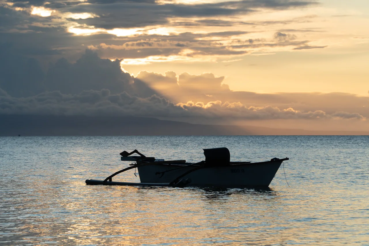 A small boat silhouetted against the sunset sea at Laipori