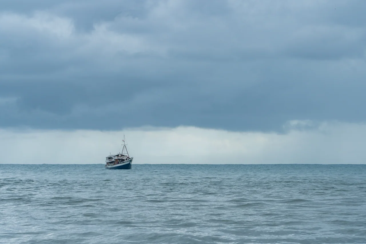 A boat offshore under a moody sky at Tarimbang