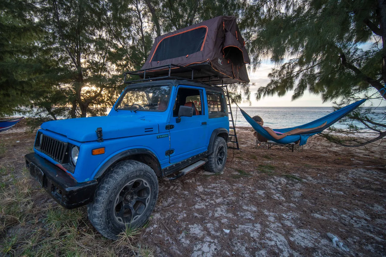 Blue vintage Jeep with rooftop tent in a shaded coastal camp