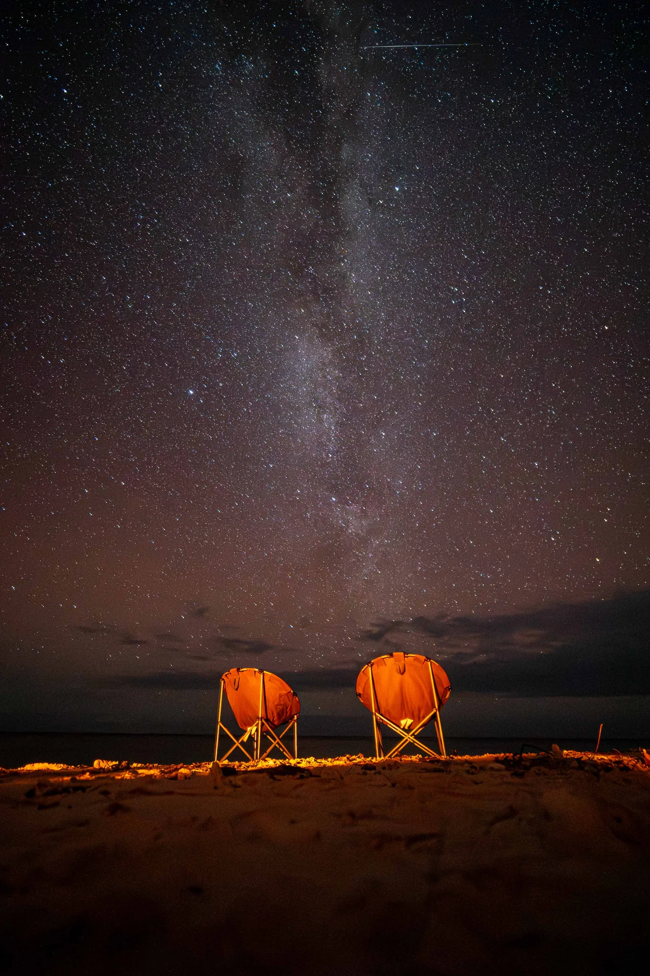 Two camping chairs beneath the Milky Way beside the coast