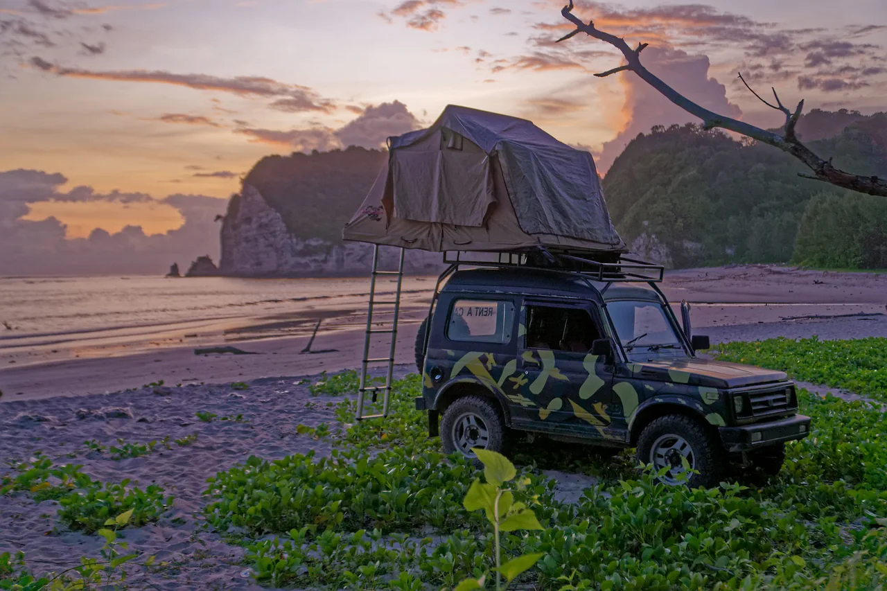 Vintage camouflage Jeep with rooftop tent beside the coast at sunset